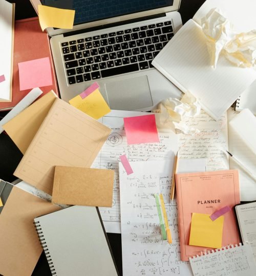 Flatlay of a messy study desk with laptop, notebooks, and sticky notes, showcasing the creative process.