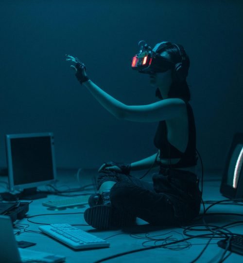 Woman immersed in virtual reality, surrounded by tech, in a dimly lit room.